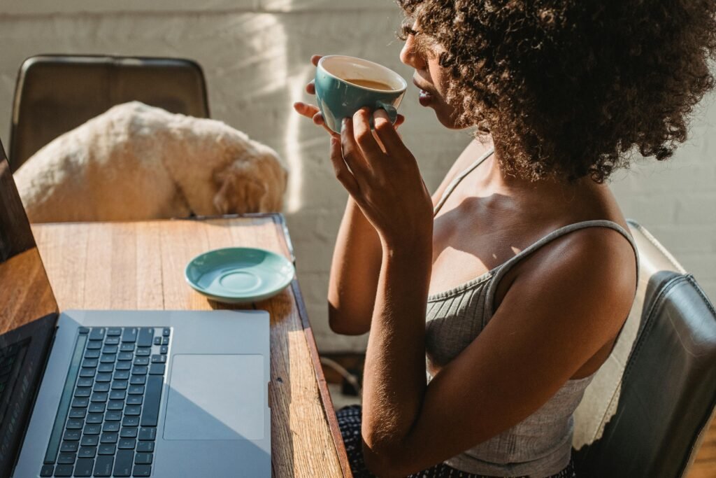 Woman enjoying coffee while working on her laptop at the table in her home content studio.